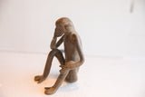 Profile view of a vintage sitting monkey figurine with a textured, aged surface.