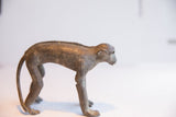 The textured, aged surface and form of a vintage monkey figurine from a side view.