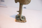 A close view of the rooster sculpture's spurred legs and weathered square base.