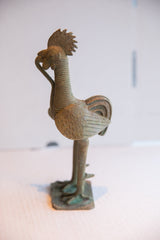 Side profile of a vintage African rooster sculpture with a snake and textured bronze patina.