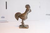 Vintage African rooster sculpture in profile, with a ribbed neck, textured body, and fanned tail.