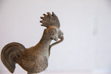 The textured, patinated head of a handmade African rooster sculpture with a ribbed neck.