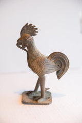 Profile view of a vintage African rooster sculpture with a textured, aged metal finish.