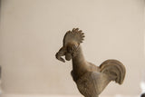 Side view of the rooster sculpture's head showing its textured comb and spiral eye.