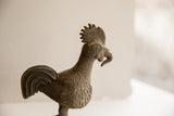 Profile view of the vintage rooster's sculpted head, showing the ribbed neck and spiral eye.