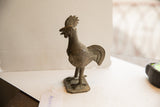 Vintage African rooster sculpture, showing its textured head, ringed neck, and aged patina.