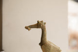 Profile detail of the African bird sculpture's head, featuring a spiral eye and a fish in its beak.