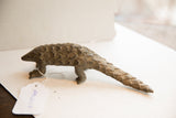 Side view of the rustic African pangolin sculpture with its white paper tag.