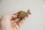 A hand holding a small vintage fish figurine, showcasing its rustic, handmade charm.