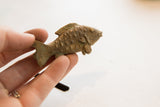 A small, vintage African fish figurine held in hand, showing its textured, patinated finish.
