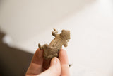 Side profile of a small, rustic handmade African frog figurine held in hand.