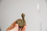 Hand holding vintage African coiled snake figurine, showcasing its textured body and green patina.
