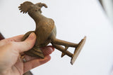 Detail of the vintage African rooster sculpture's textured tail and spurred legs.