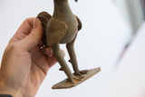 Vintage African rooster sculpture's textured aged metal legs and base held in hand.