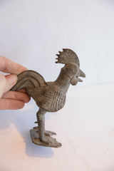 A hand holding the vintage African rooster sculpture to show its scale and texture.