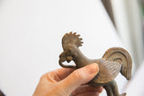 Profile view of a collectible African rooster figure with a textured, time-softened patina.