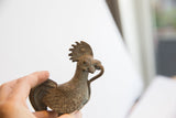 A hand holding the vintage rooster sculpture, showing a detailed profile and aged patina.
