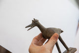 Vintage African bird casting held in hand, revealing its textured, dark metal finish.