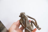 A hand holds the vintage monkey figurine, showing its pensive pose and rustic texture.