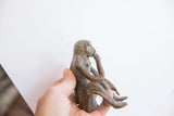A hand holds the vintage monkey figurine, showing its scale and aged texture.