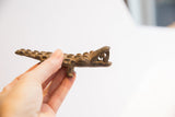 Handheld view of a vintage alligator sculpture showing its textured side and open jaws.