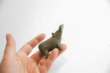 A hand holding the small vintage hippo figurine to show its scale and oxidized finish.