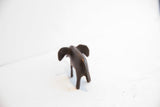 Vintage dark patina elephant figurine shown from the back with ears splayed.