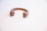 Geometric carvings on the faceted, blocky ends of an antique copper cuff bracelet.