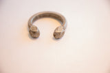 Full view of a handmade African aluminum cuff showing its open shape and textured patina.