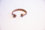 Three-quarter view of the antique copper cuff showing the opening between its faceted ends.