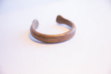 The thick, C-shaped curve of the antique African copper bracelet with a warm patina.