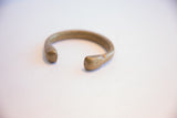 Smooth, rounded terminals of an antique bronze cuff showing an aged patina.