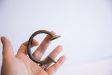 A hand holds the antique African manilla cuff, highlighting its scale and dark patina.
