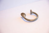 Angled view of an antique Manilla cuff showing its C-shape and aged metal patina.