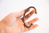 The rustic, twisted form of a vintage African cuff bracelet held to show scale.