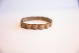 Three-quarter view of a vintage African bracelet with scalloped floral-stamped segments.