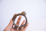 Vintage bronze-toned African cuff held to show its rounded shape and scale.