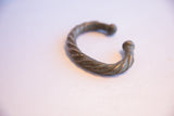 The curved form and handmade twist design of an antique African oxidized cuff.