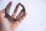 Vintage copper alloy cuff held to show its C-shape profile and aged patina.