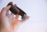 A hand holding the antique African cuff, showing its substantial, sculptural form.
