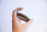 A hand holding the vintage bronze cuff, showing its substantial form and etched patterns.
