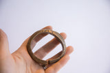 Vintage bronze African cuff with a worn patina and carved details held in hand.