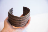 Hand holding the vintage African wide cuff to show its scale and riveted metal design.