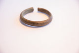 The thick, rounded form of a vintage African cuff with an oxidized, lined texture.