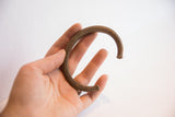 A hand holding the vintage African cuff bracelet to show its scale and C-shape.