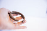 Hand-held view showing the open C-shape and notched texture of a vintage African cuff.