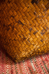 Antique bamboo basket's rich, textured diagonal weave resting on a red patterned rug.