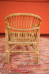 Mid Century Modern rattan chair back with vertical slats and woven details on a braided red rug.