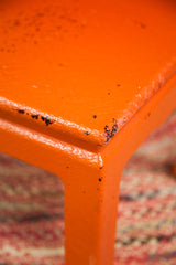 Vintage orange painted wicker table corner, showing worn, chipped finish.