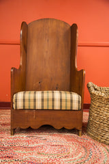 Detail of the antique settle chair's wide wooden back and plaid upholstered seat.